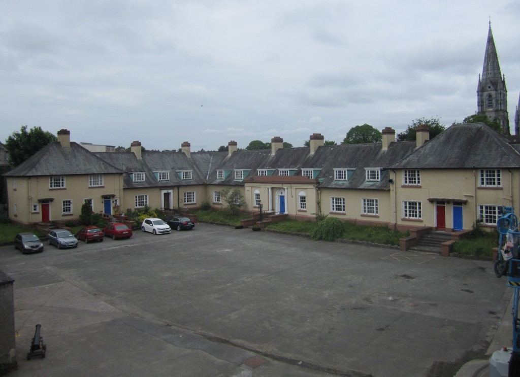 Image of the interior of Elizabeth Fort, Cork, showing and open air square with parked cars surrounded by two story buildings.